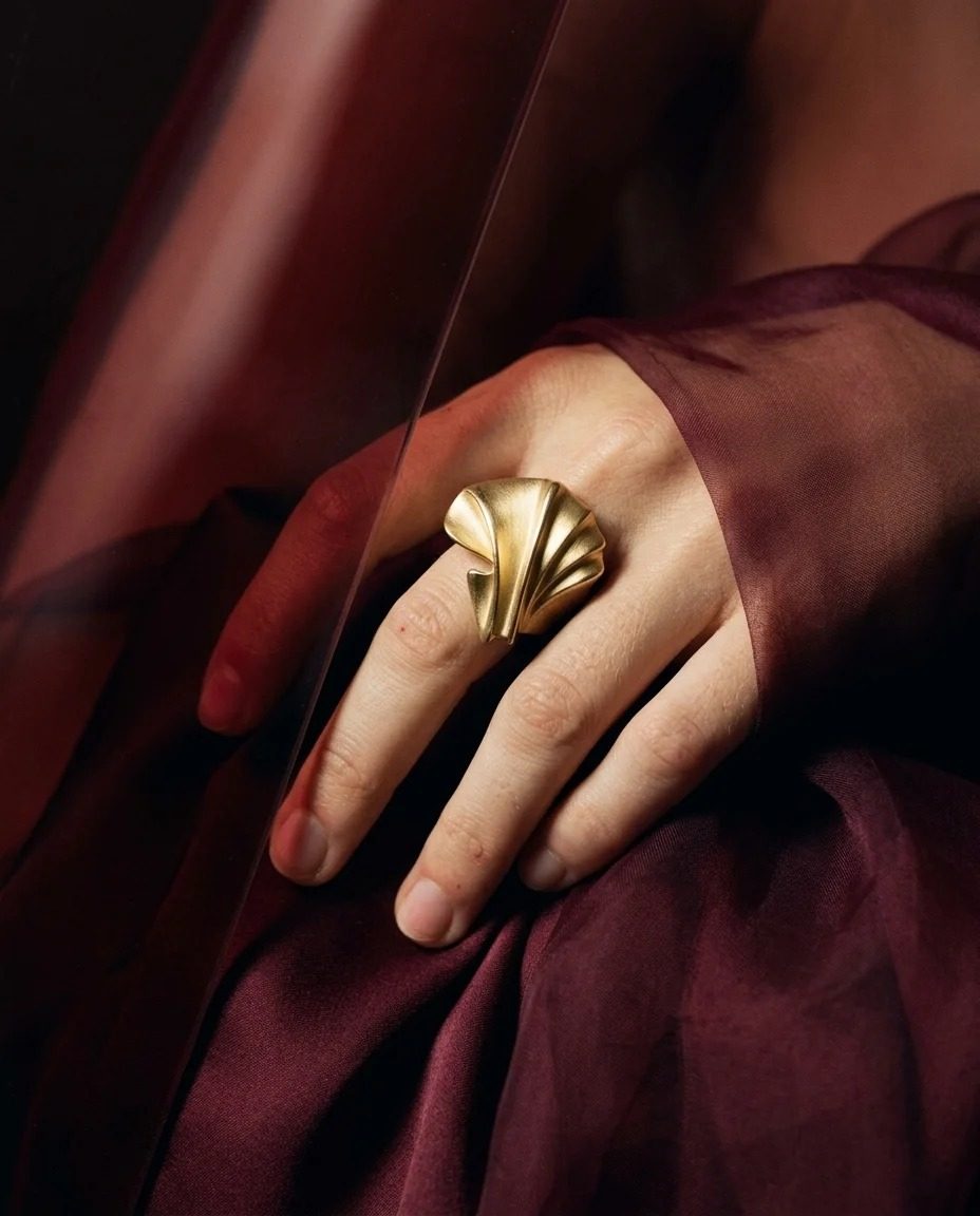 VELORA fan ring on a hand resting on oxblood silk